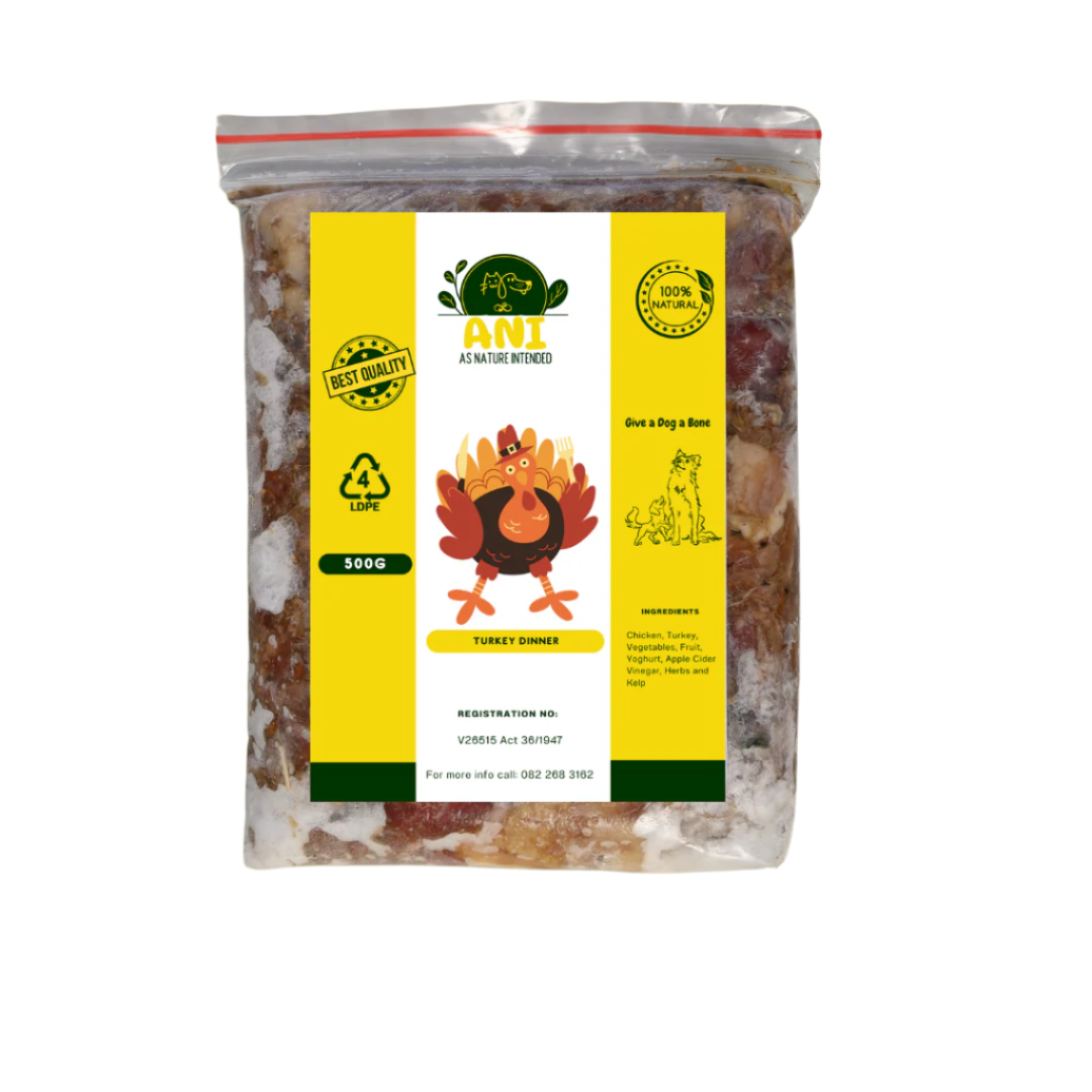 A bag of dog food branded 'Turkey Dinner' from As Nature Intended, surrounded by images of raw turkey meat, vegetables, and fruit on a wooden table against a yellow background with green leaves.